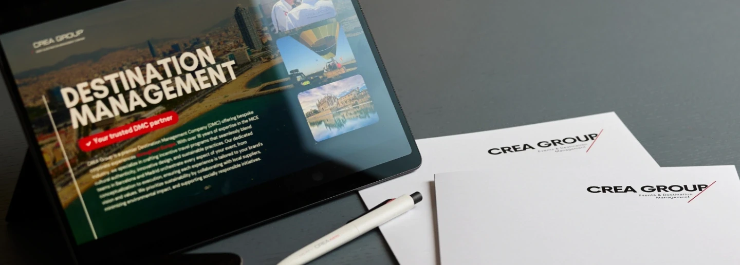 Mesa de reunión con una tablet que muestra la pantalla de Destination Management de CREA Group, acompañada de carpetas corporativas, tarjetas de visita, un bolígrafo y un teléfono móvil.