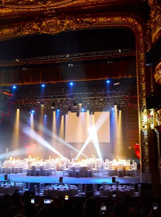 Vista panorámica de una cena de gala montada en el escenario de un teatro histórico con iluminación dramática.