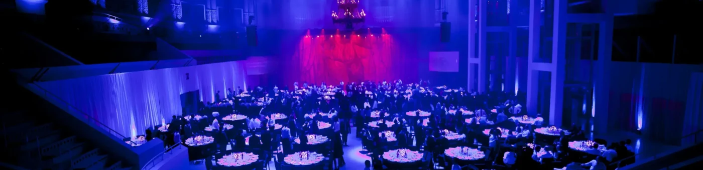 Vista panorámica de una cena de gala corporativa con iluminación vibrante en rosa y púrpura.