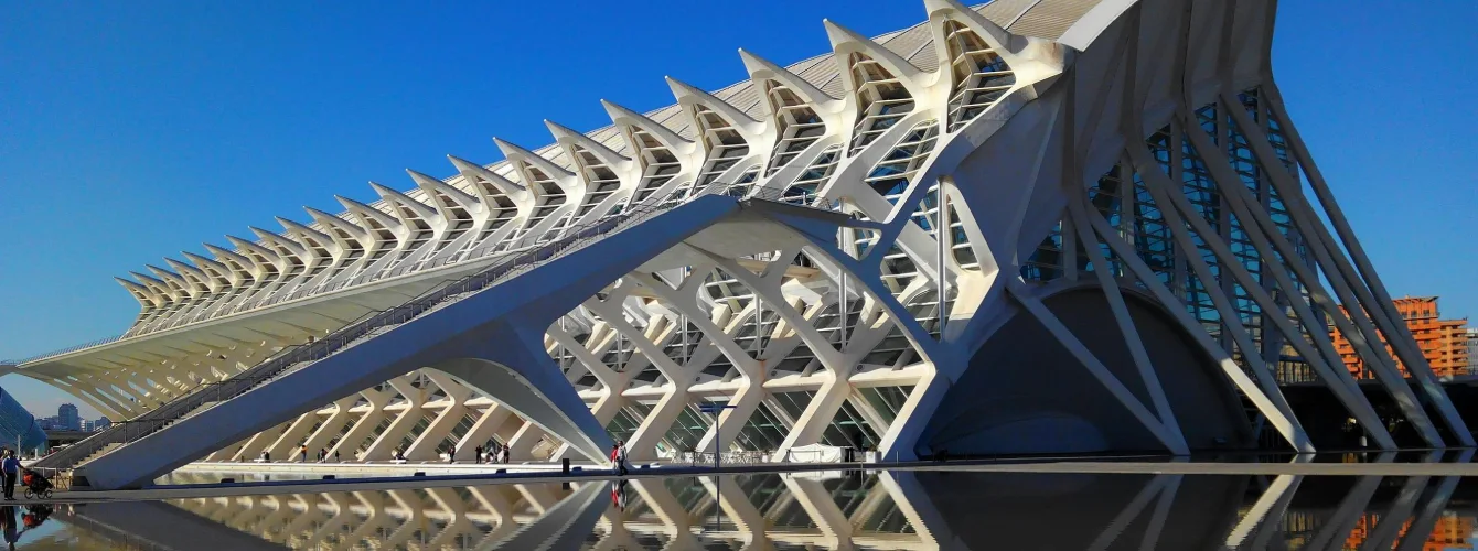 Daytime view of the Prince Philip Science Museum in Valencia’s City of Arts and Sciences, featuring its futuristic white structure with arches and rib-like beams reflected in the water under a deep blue sky