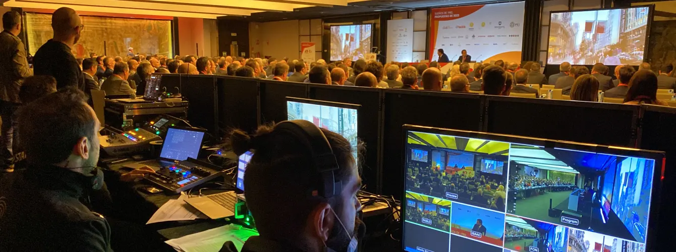 Large audience attending Wall Street English conference session with speakers on stage, multiple screens displaying program, and technical setup in foreground
