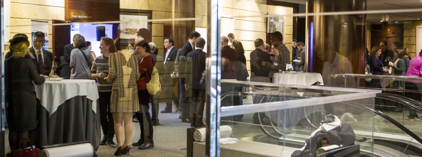 Professional networking crowd at Wall Street English event mingling in a modern conference venue with escalators and attendees in business attire