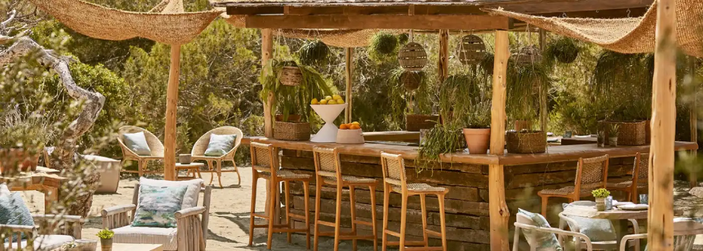 Bohemian outdoor terrace bar in Mallorca with wooden counter straw shades hanging plants and natural garden setting