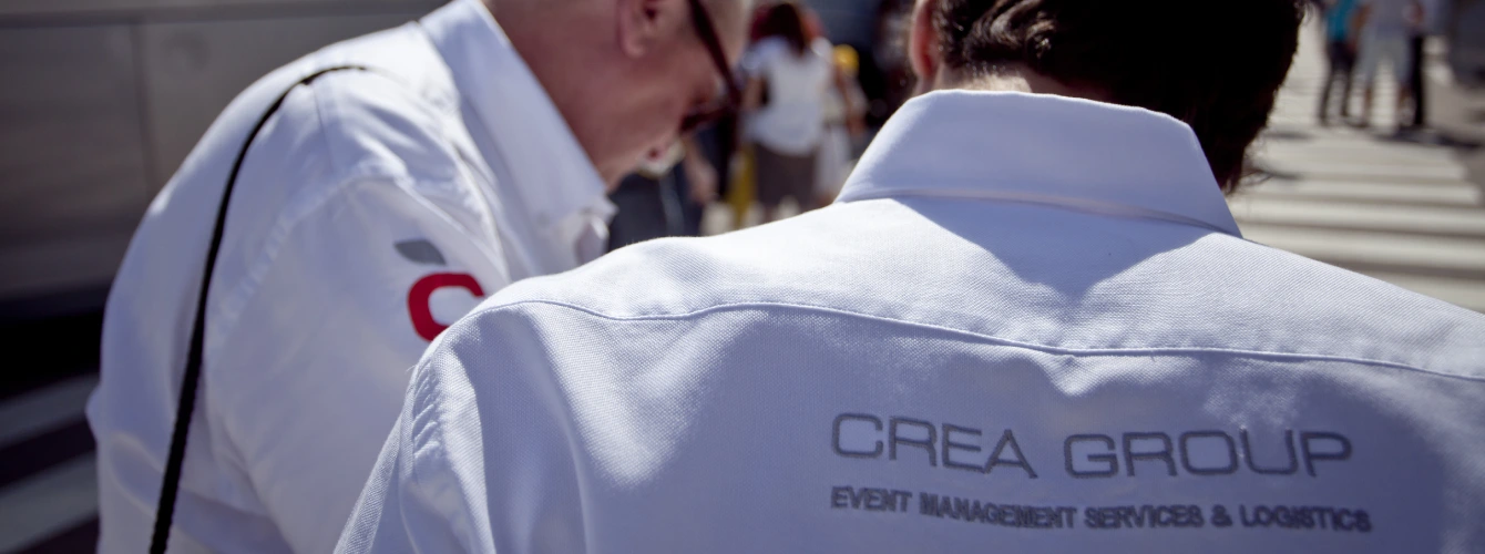 Close-up of the CREA Group logo embroidered on a professional white staff shirt for event logistics.