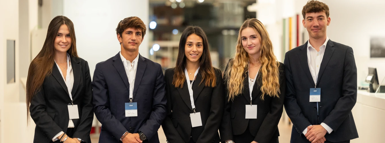 A team of five professional event hosts in formal business attire with accreditation badges.