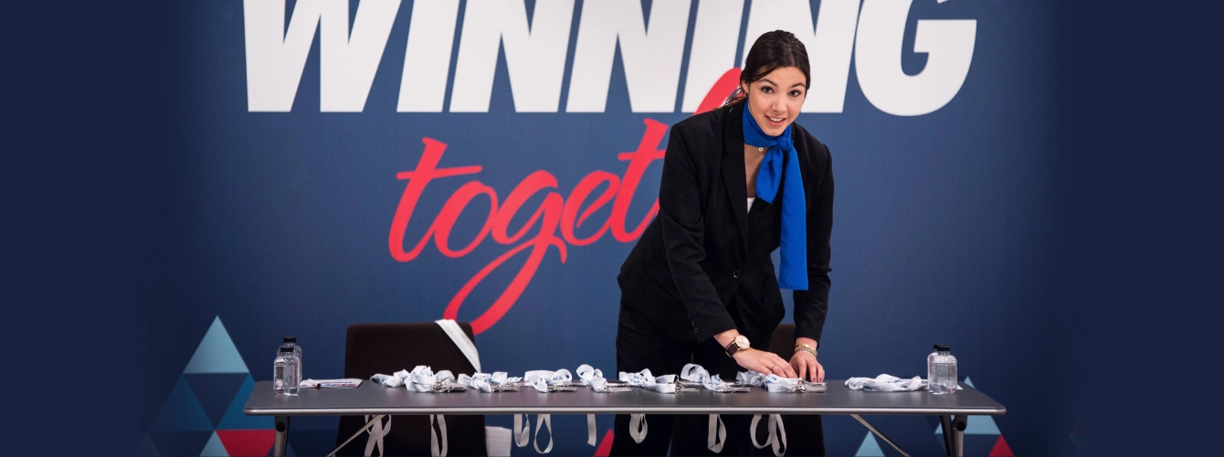 Event hostess organizing attendee lanyards on a table in front of a "Winning Together" backdrop.