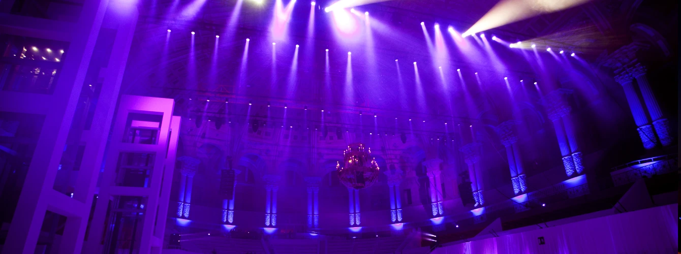 Grand venue interior with dramatic purple spotlighting and a large chandelier during a high-end corporate event.