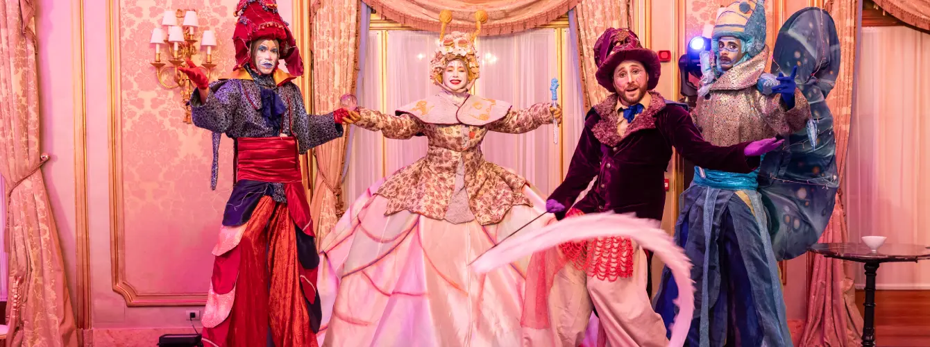 Four entertainers in elaborate, colorful fantasy costumes posing at a luxury gala event.