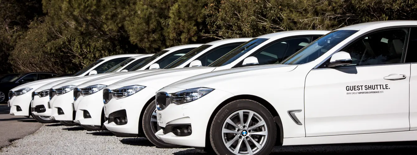 Row of silver Mercedes-Benz executive cars parked at an airport terminal for event attendee transfers.