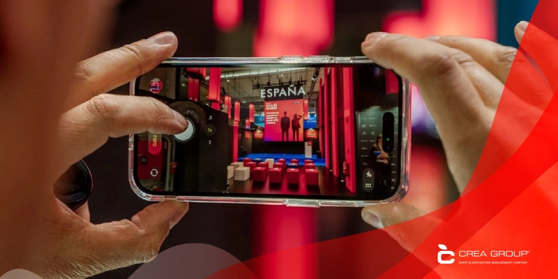 Close-up of a person capturing a photo with a smartphone of the Spain Pavilion stage at MWC Barcelona 2026, featuring red architectural elements and professional event branding.