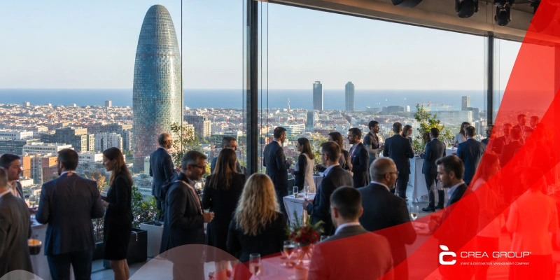 Attendees enjoying a networking cocktail reception on an outdoor rooftop terrace with a panoramic view of Barcelona and the Torre Glòries skyscraper in the backgrou