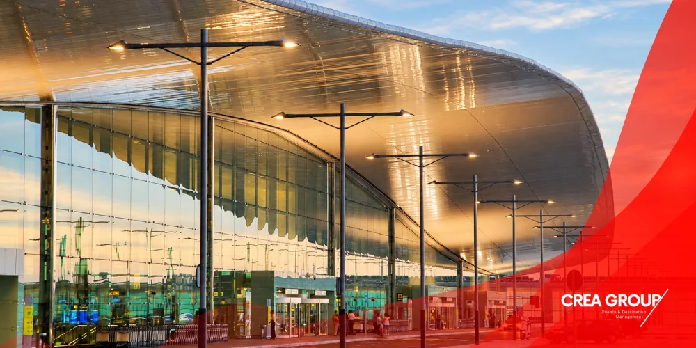 Vista exterior de la Terminal 1 del Aeropuerto Josep Tarradellas Barcelona-El Prat al atardecer, con su fachada de cristal y techo curvo.